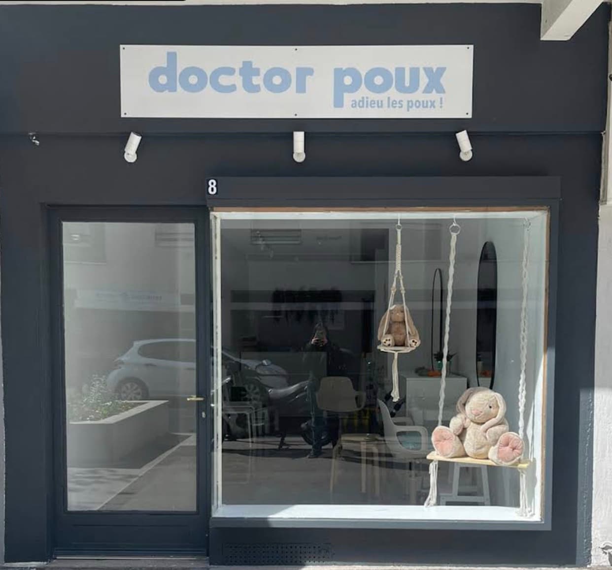 La devanture du centre d’Annemasse : l’enseigne « doctor poux, adieu les poux ! » et deux lapins en peluche sur une balançoire en macramé dans la vitrine.